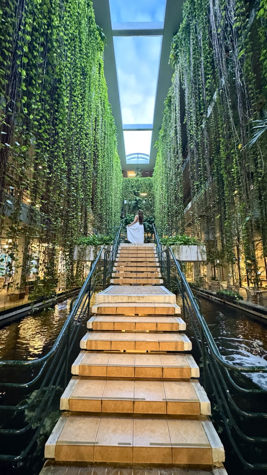 Jennifer ascending a staircase surrounded by hanging greenery